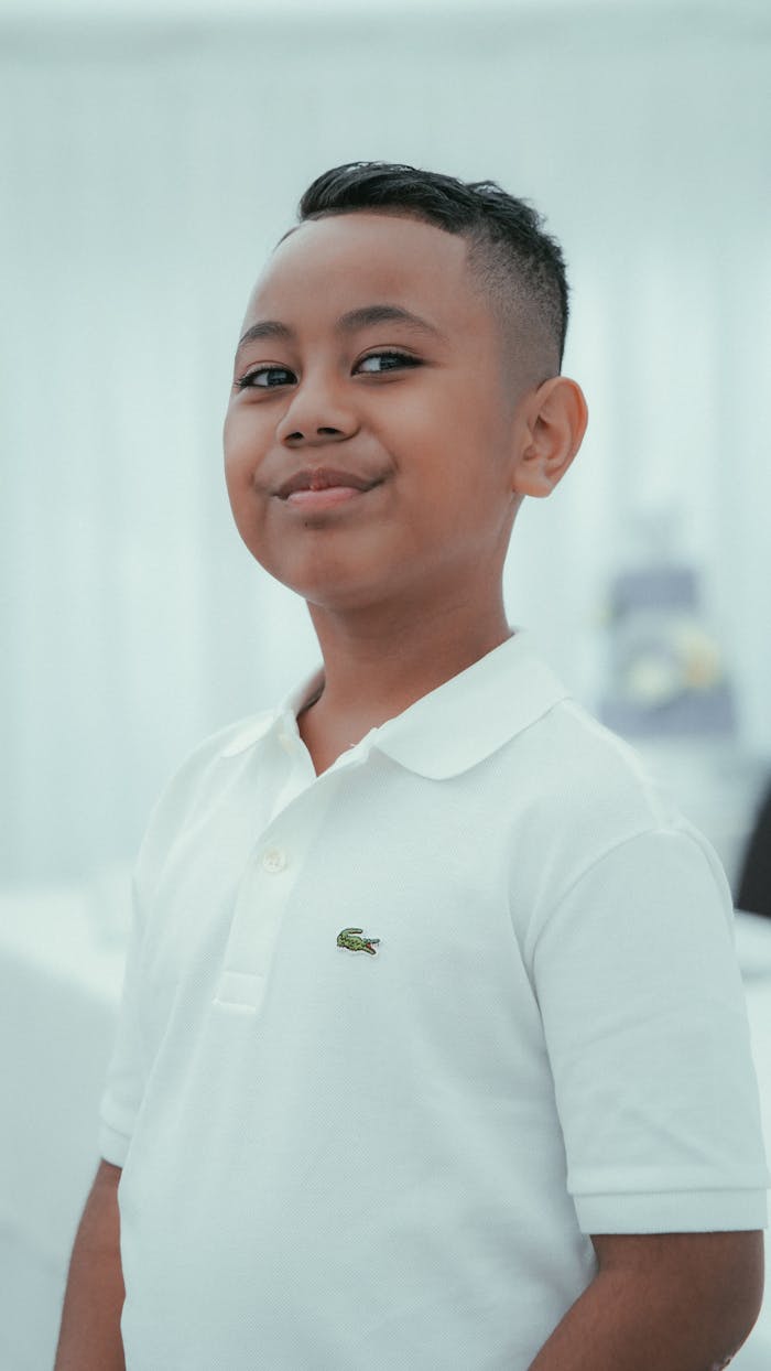 Young boy smiling confidently, wearing a white polo shirt, in a bright setting.